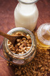 Crunchy muesli in a jar, honey and milk bottle beside it