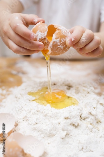 Photo: Child breaking an egg onto a heap of flour Child breaking an egg onto a heap of flour