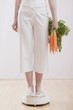 Young woman with carrots on bathroom scales