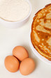 Pile of pancakes with some flour and eggs on white background Pile of pancakes with some flour and eggs on white background