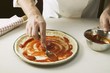 Foto: Spreading pizza base with tomato sauce Spreading pizza base with tomato sauce