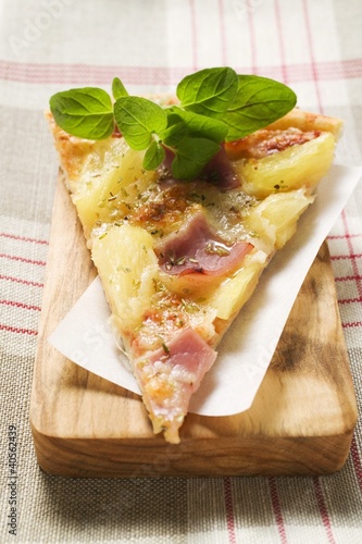 Foto: Slice of Hawaiian pizza with fresh oregano on chopping board Slice of Hawaiian pizza with fresh oregano on chopping board