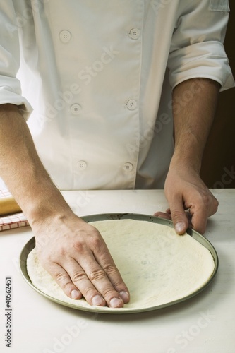 Photo: Pressing pizza dough into baking tin Pressing pizza dough into baking tin