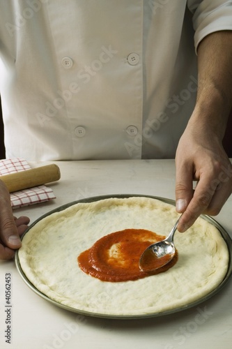 Photo: Spreading pizza dough with tomato sauce Spreading pizza dough with tomato sauce