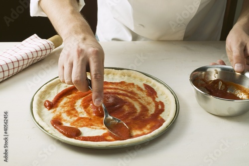 Photo: Spreading pizza base with tomato sauce Spreading pizza base with tomato sauce