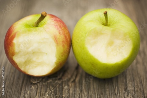 Photo: Two apples with bites taken on wooden background Two apples with bites taken on wooden background
