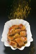 Sprinkling curry powder over sausage in paper dish