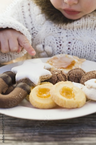 Photo: Small girl reaching for Christmas biscuit on plate Small girl reaching for Christmas biscuit on plate