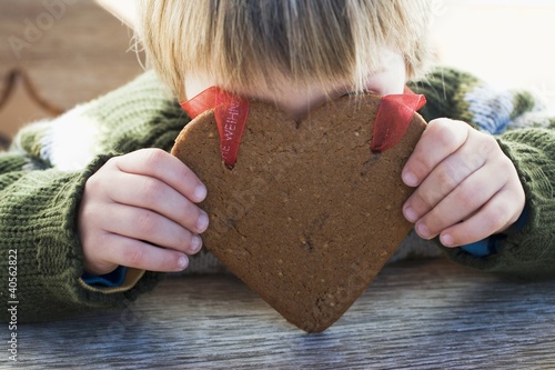 Photo: Small boy holding gingerbread heart in front of his face Small boy holding gingerbread heart in front of his face