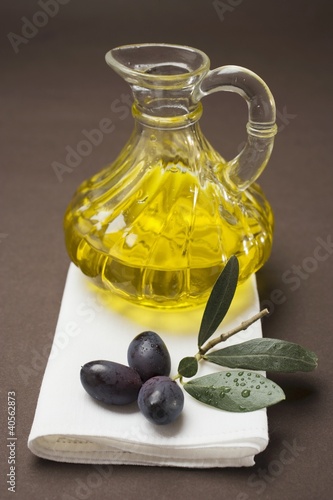 Photo: Olive sprig with black olives, carafe of olive oil behind Olive sprig with black olives, carafe of olive oil behind