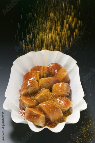 Photo: Sprinkling curry powder over sausage in paper dish Sprinkling curry powder over sausage in paper dish