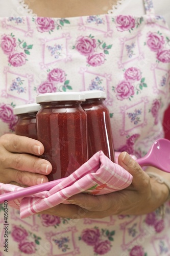 Photo: Woman holding jars of jam, tea towel and kitchen spoon Woman holding jars of jam, tea towel and kitchen spoon