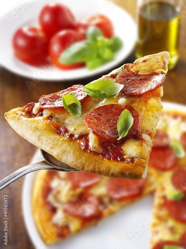 Photo: Slice of pepperoni pizza with basil on server Slice of pepperoni pizza with basil on server