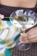 Foto: Woman holding green olive on cocktail stick over Martini glass Woman holding green olive on cocktail stick over Martini glass