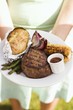 Woman holding a plate of grilled steak and accompaniments