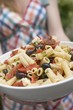 Foto: Woman holding large dish of pasta salad with olives & tomatoes Woman holding large dish of pasta salad with olives & tomatoes