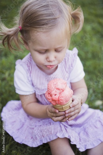 Foto: Small girl sitting on grass, holding strawberry ice cream cone Small girl sitting on grass, holding strawberry ice cream cone