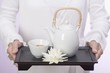 Woman holding teapot, tea bowl and water lily on tray