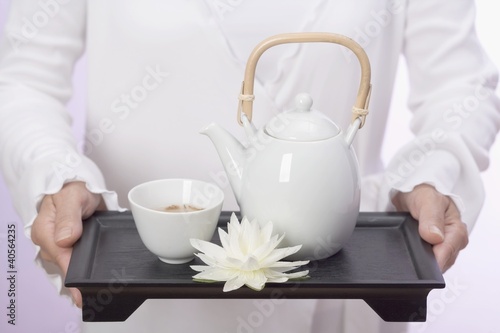 Photo: Woman holding teapot, tea bowl and water lily on tray Woman holding teapot, tea bowl and water lily on tray