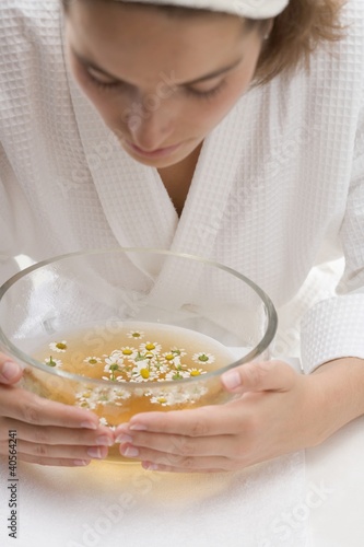 Photo: Woman bending over bowl of chamomile tea with flowers Woman bending over bowl of chamomile tea with flowers