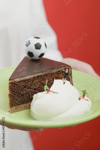 Photo: Person holding piece of Sacher torte with cream & football Person holding piece of Sacher torte with cream & football