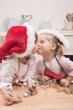 Two small girls in Father Christmas hats kissing in kitchen