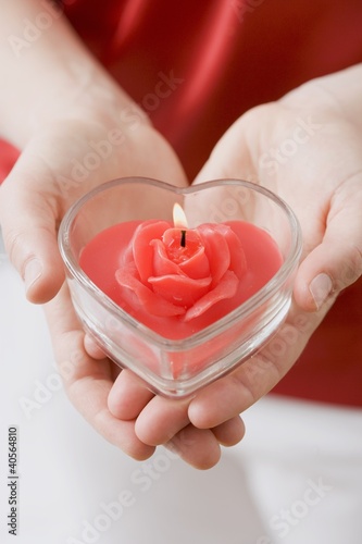 Photo: Hands holding heart-shaped windlight with rose candle Hands holding heart-shaped windlight with rose candle