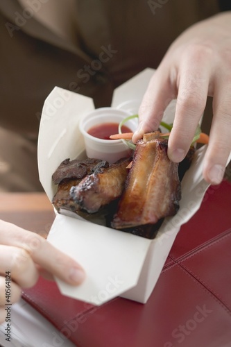 Photo: Woman taking glazed pork rib out of take-away container Woman taking glazed pork rib out of take-away container