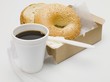 Sesame bagel with crème fraîche in cardboard box, cup of coffee