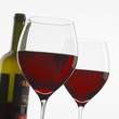 Two glasses of red wine in front of bottle