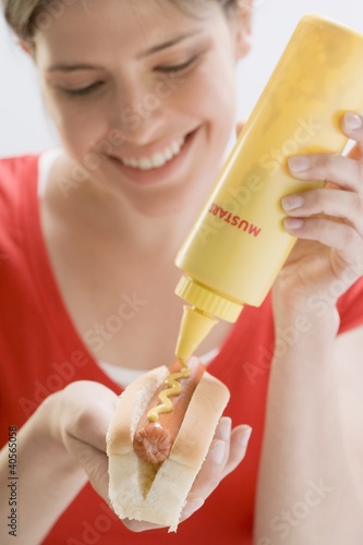 Photo: Young woman putting mustard on hot dog Young woman putting mustard on hot dog