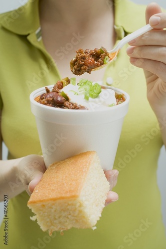 Photo: Woman holding chili con carne in paper cup and cornbread Woman holding chili con carne in paper cup and cornbread