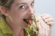 Foto: Woman biting into a sandwich with enjoyment Woman biting into a sandwich with enjoyment