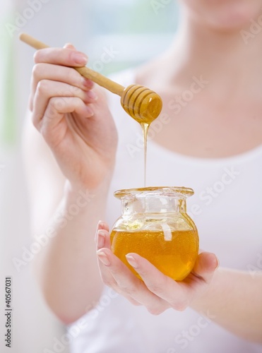 Photo: Young woman holding jar of honey and honey dipper Young woman holding jar of honey and honey dipper