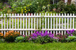 White picket fence surrounded by garden flowers in yard