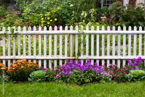 Photo: White picket fence surrounded by garden flowers in yard White picket fence surrounded by garden flowers in yard