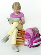 Pupil seated on books plays concentrated with tabletpc