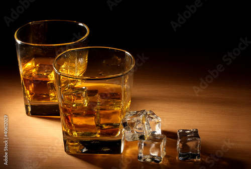 Photo: two glasses of scotch whiskey and ice on wooden table two glasses of scotch whiskey and ice on wooden table