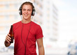 portrait of young man listening music and holding beer against a