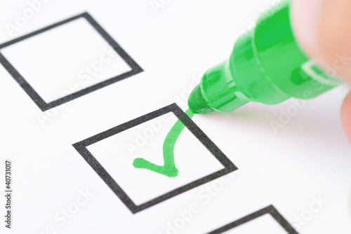 Foto: Macro shot of human hand drawing green check mark in checklist b Macro shot of human hand drawing green check mark in checklist b