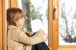 Young Girl Sitting On Window Ledge Looking At Snowy View
