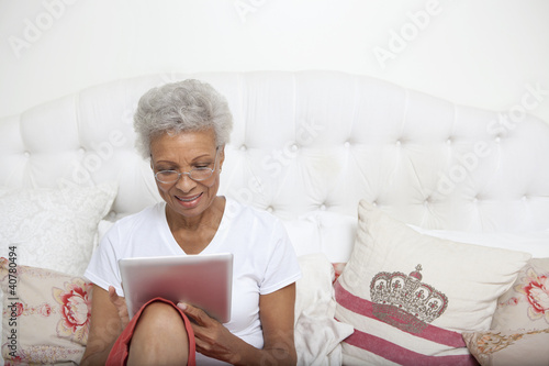 Photo: Older woman using tablet computer in bed Older woman using tablet computer in bed