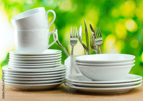 Photo: Clean dishes on wooden table on green background Clean dishes on wooden table on green background