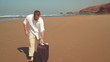 Young man with valise standing on the beach, steadicam shot