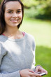 canvas print picture - Smiling young woman using her cellphone while standing in a park