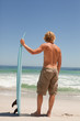 Young blonde man holding his surfboard in front of the ocean