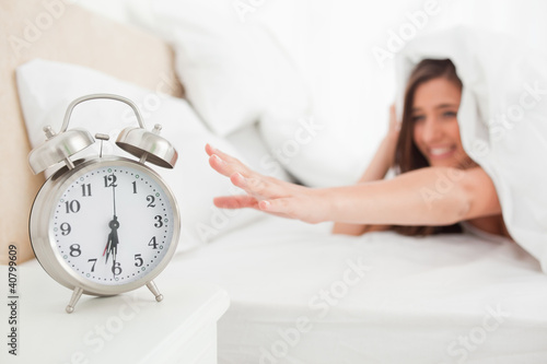 Photo: Woman under the quilt reaches for the clock Woman under the quilt reaches for the clock