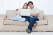 A smiling couple with a laptop are looking at the camera
