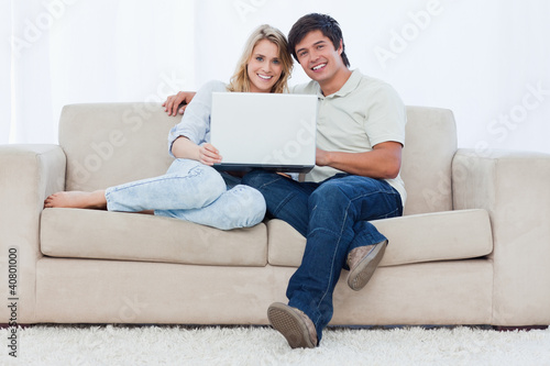 Photo: A smiling couple with a laptop are looking at the camera A smiling couple with a laptop are looking at the camera