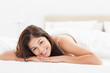 Photo: Woman lying on the bed, looking forward and smiling with her hea Woman lying on the bed, looking forward and smiling with her hea